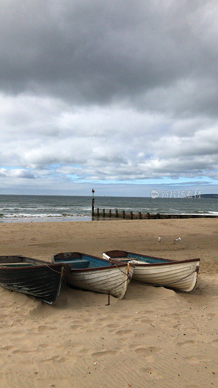 三艘划艇/渔船在沙滩上排成一排，背景是海岸线和晴朗的夏日天空，白色和黑色的渔民木船在海边，以防止海水侵蚀和海鸥，复制空间